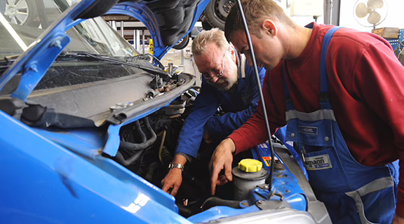 Wir bereiten Ihr Fahrzeug sorgfältig auf die Hauptuntersuchung vor. Zwei Mechaniker untersuchen Motorraum von Auto